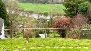 Un paysage rural avec une rivière, des champs verdoyants et une maison dotée d’un jardin.
