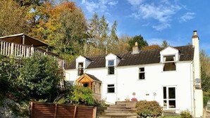 Une maison blanche à deux étages, dotée d’un toit en pente, d’une terrasse en bois et d’une pelouse bien entretenue.
