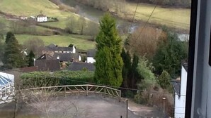 Une vue depuis une fenêtre donnant sur une vallée, avec une rivière, des maisons et une colline.