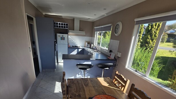 Een moderne keuken met een centraal eiland, een eethoek met een houten tafel en stoelen, en uitzicht op een tuin door een groot raam.