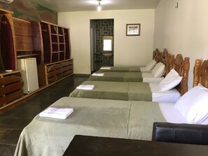 A hotel room with four beds aligned in a row, a small sink, and a wooden cabinet.