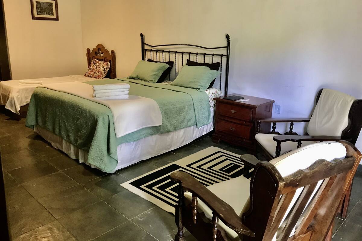 Un dormitorio con dos camas, una mesita de noche, una silla y una alfombra estampada.