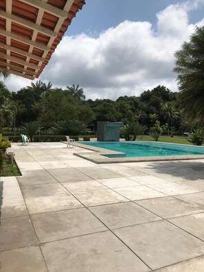 A swimming pool with a tiled deck, surrounded by lush greenery and palm trees.