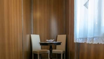 A corner room with wooden panel walls, a wooden floor, two chairs, a small table, and a window with a white curtain.