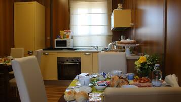 A hotel room with a dining area featuring a table set with breakfast items, a microwave, and a small kitchenette.