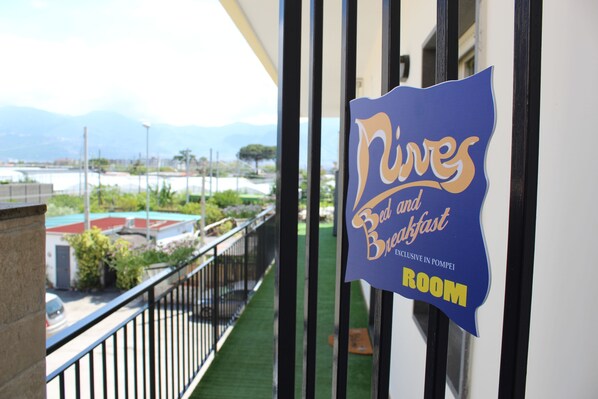 Señal para 'Nives Bed and Breakfast' con vista a un balcón y un paisaje distante.