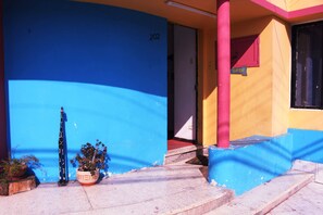 A building with a blue and yellow facade, a number '202' on the wall, and a red door. - Hostel La Posada De Gallo (Arica)
