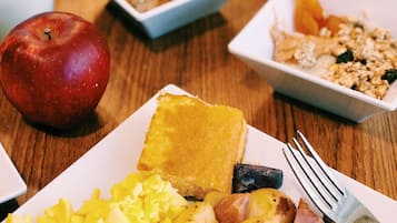 Ein Frühstückstisch mit verschiedenen Speisen, darunter Rührei, Speck, Toast und Obst.