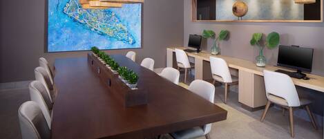 A modern meeting room with a long table, white chairs, a large abstract painting, a computer desk, and a television.