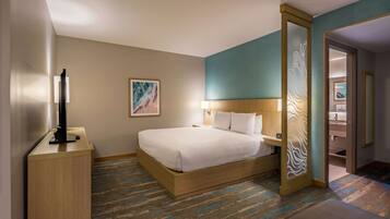 Une chambre d’hôtel avec un lit, une table de chevet, une lampe, une œuvre d’art et une vue sur la salle de bain.