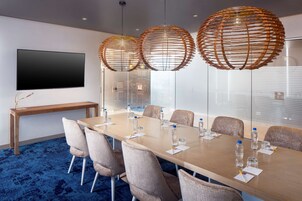 Un salón de conferencias con una mesa larga, sillas, un televisor y tres lámparas esféricas colgantes.