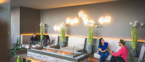 A modern lobby with a glass-top fireplace, seating area, and decorative wall lighting.