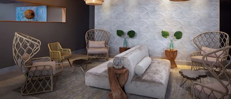 A modern lounge area with wicker chairs, a large sectional sofa, and two potted plants.