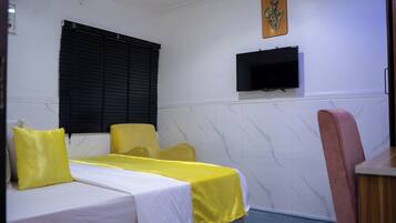 A hotel room with two single beds, a television mounted on the wall, and a window with black blinds.