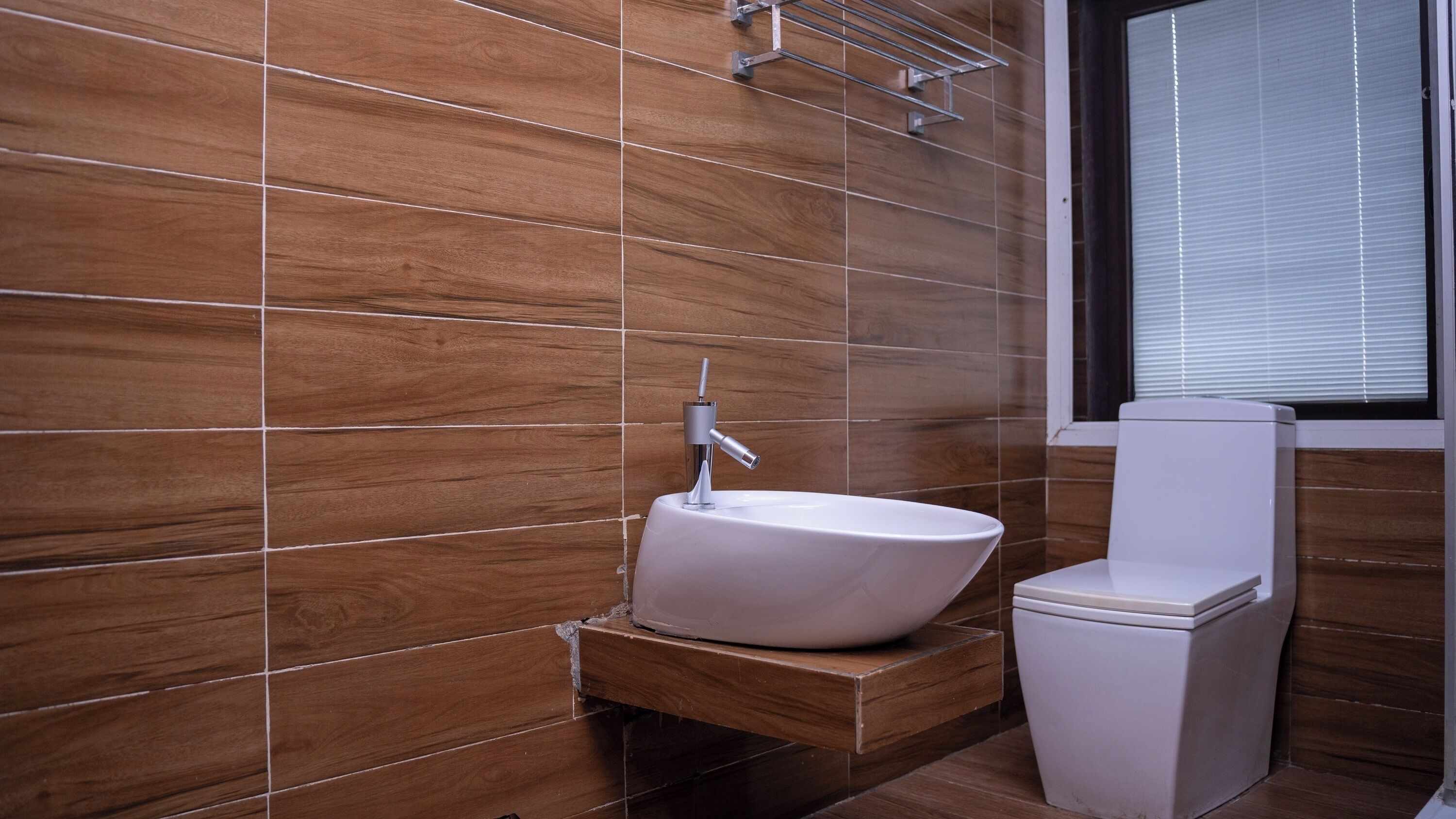 A bathroom with a white sink, a toilet, and a window with blinds.