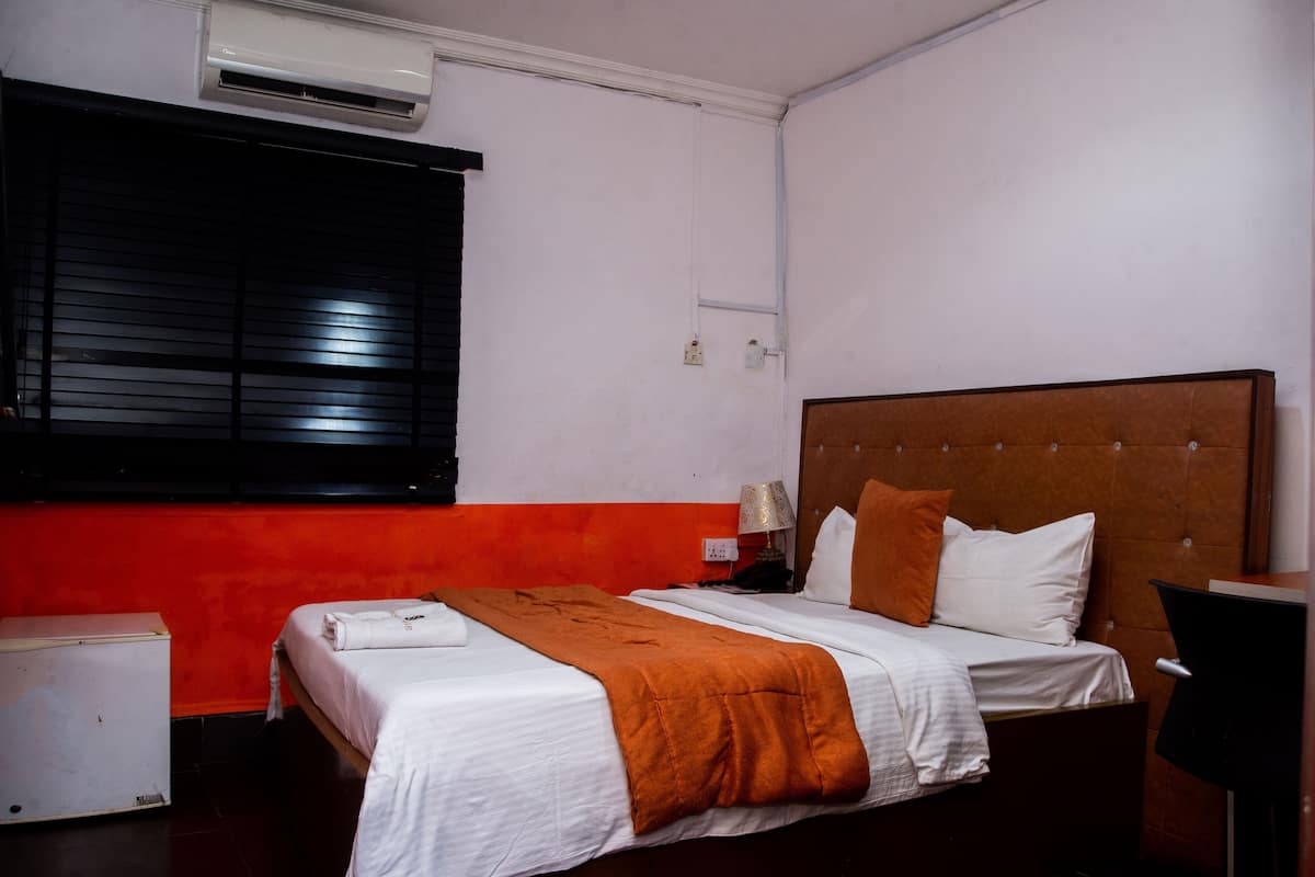 Una habitación de hotel con cama, mesita de noche, lámpara y equipo de aire acondicionado.