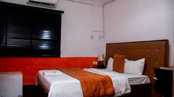 A hotel room with a bed, a nightstand, a lamp, and an air conditioning unit.