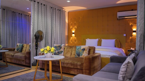 Una habitación de hotel con una cama grande, dos sofás, una pequeña mesa con flores y un equipo de aire acondicionado.