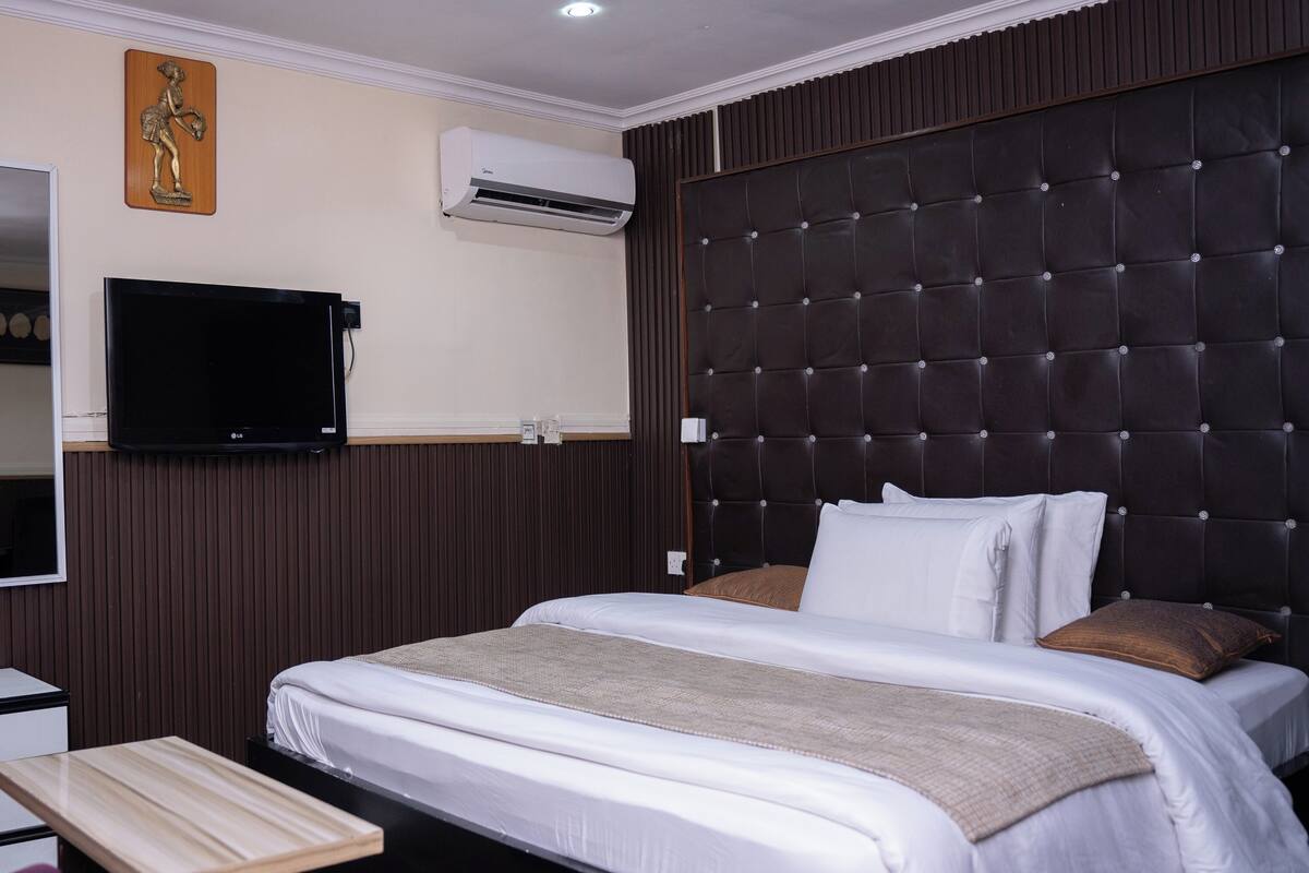 Habitación de hotel con una cama grande, una televisión de pantalla plana, un cabecero de madera y un aire acondicionado instalado en la pared.
