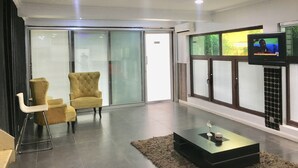 Una sala moderna con un sillón amarillo, un ventanal que da al exterior y un televisor de pantalla plana montado en la pared.