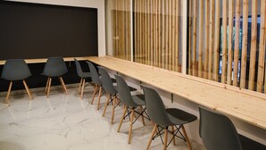 Une salle de conférence avec une longue table en bois, six chaises noires à pieds en bois et un écran noir fixé au mur.
