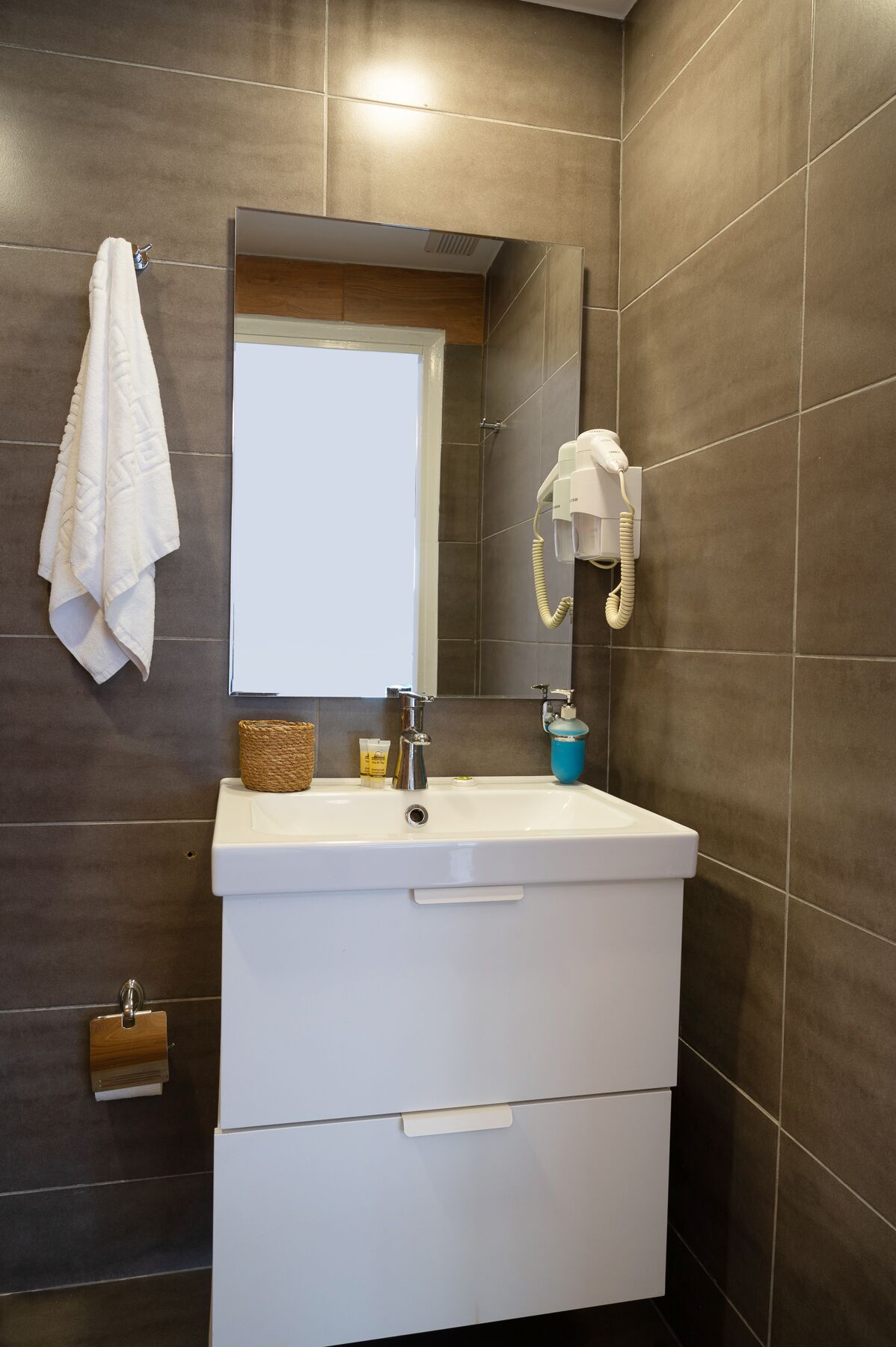 Un baño con tocador blanco, espejo, toallero, secador de pelo y dispensador de jabón.