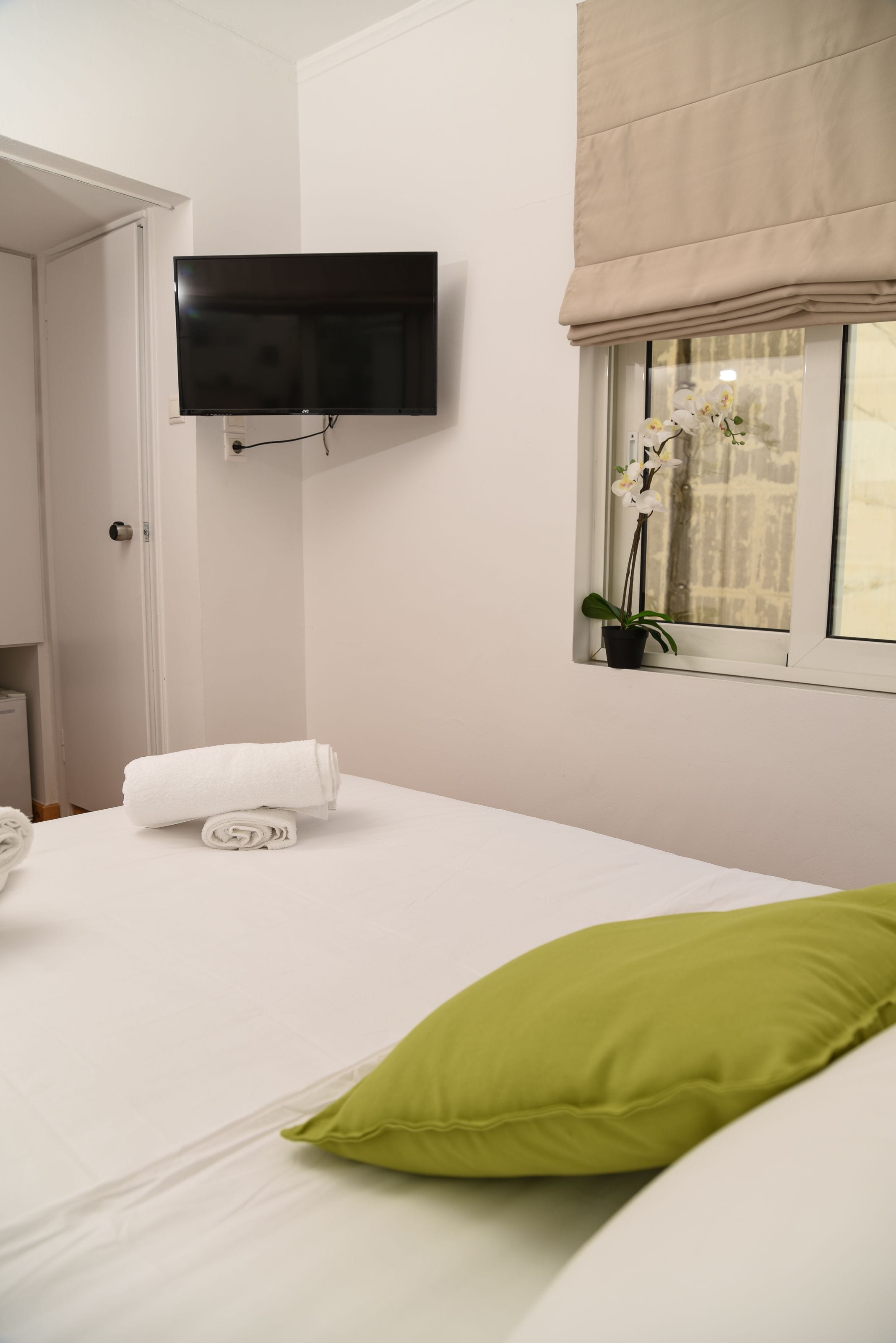Habitación de hotel con cama, televisor en la pared, ventana con vistas y una planta en el alféizar.