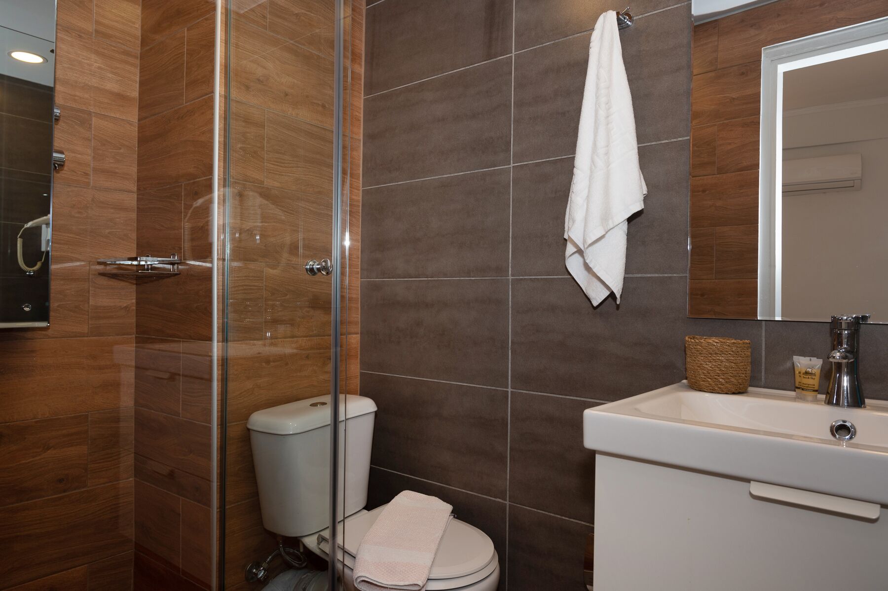 A bathroom with a glass shower enclosure, a toilet, a sink with a mirror, and a towel hanging on the wall.