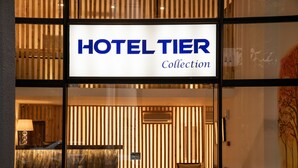 L’entrée d’un hôtel, avec une enseigne indiquant « HOTEL TIER Collection ».