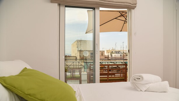 Une chambre d’hôtel avec un lit, un oreiller vert, une serviette blanche et une vue sur la ville, visible à travers une porte coulissante.