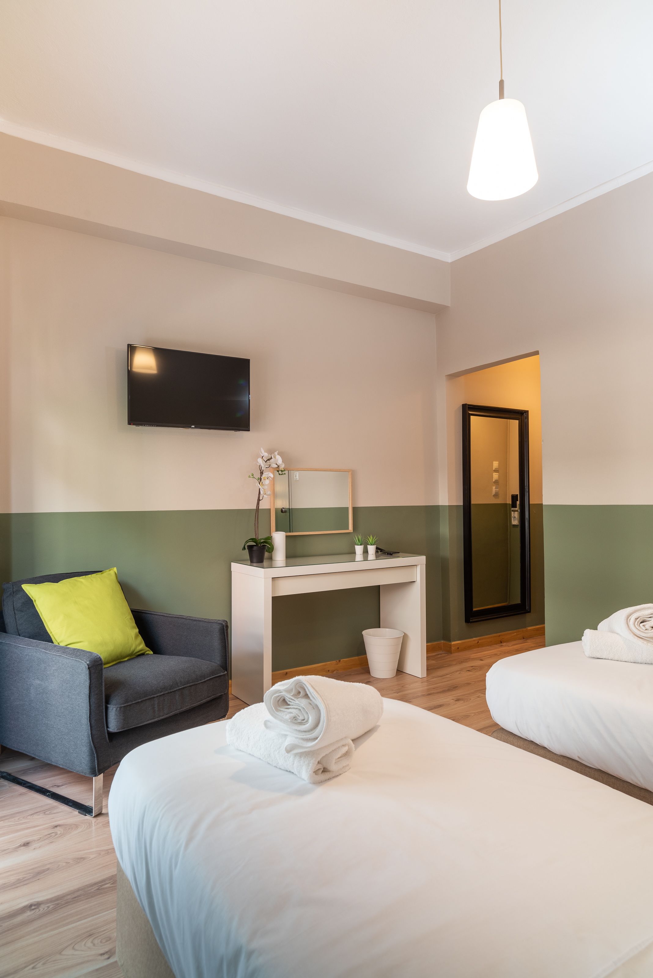 A hotel room with two beds, a desk, a chair, a television, and a mirror.