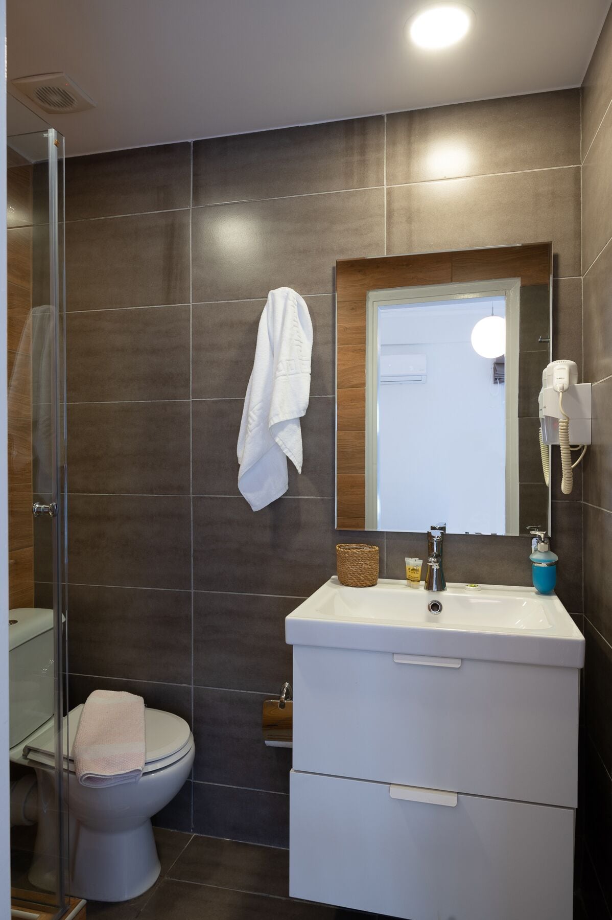 A modern bathroom with a glass shower enclosure, a toilet, a sink with a mirror above it, and a towel rack.