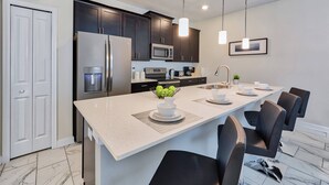 A modern kitchen with dark cabinets, stainless steel appliances, and a central island with seating. - SL4924 - 4BR house with pool near Disney (Kissimmee)
