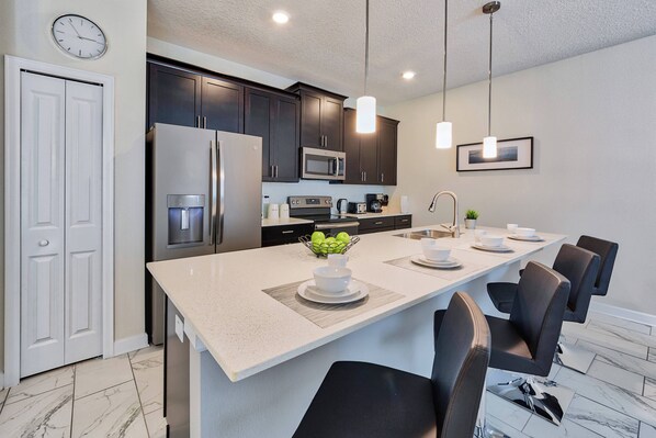 A modern kitchen with dark cabinets, stainless steel appliances, and a central island with seating. - 4924 Storey Lake Townhouse Pool | Orlando Rental (Kissimmee)