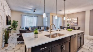 A modern kitchen with a central island, dark cabinetry, and a dining area with a sofa and chairs. - SL4924 - 4BR house with pool near Disney (Kissimmee)