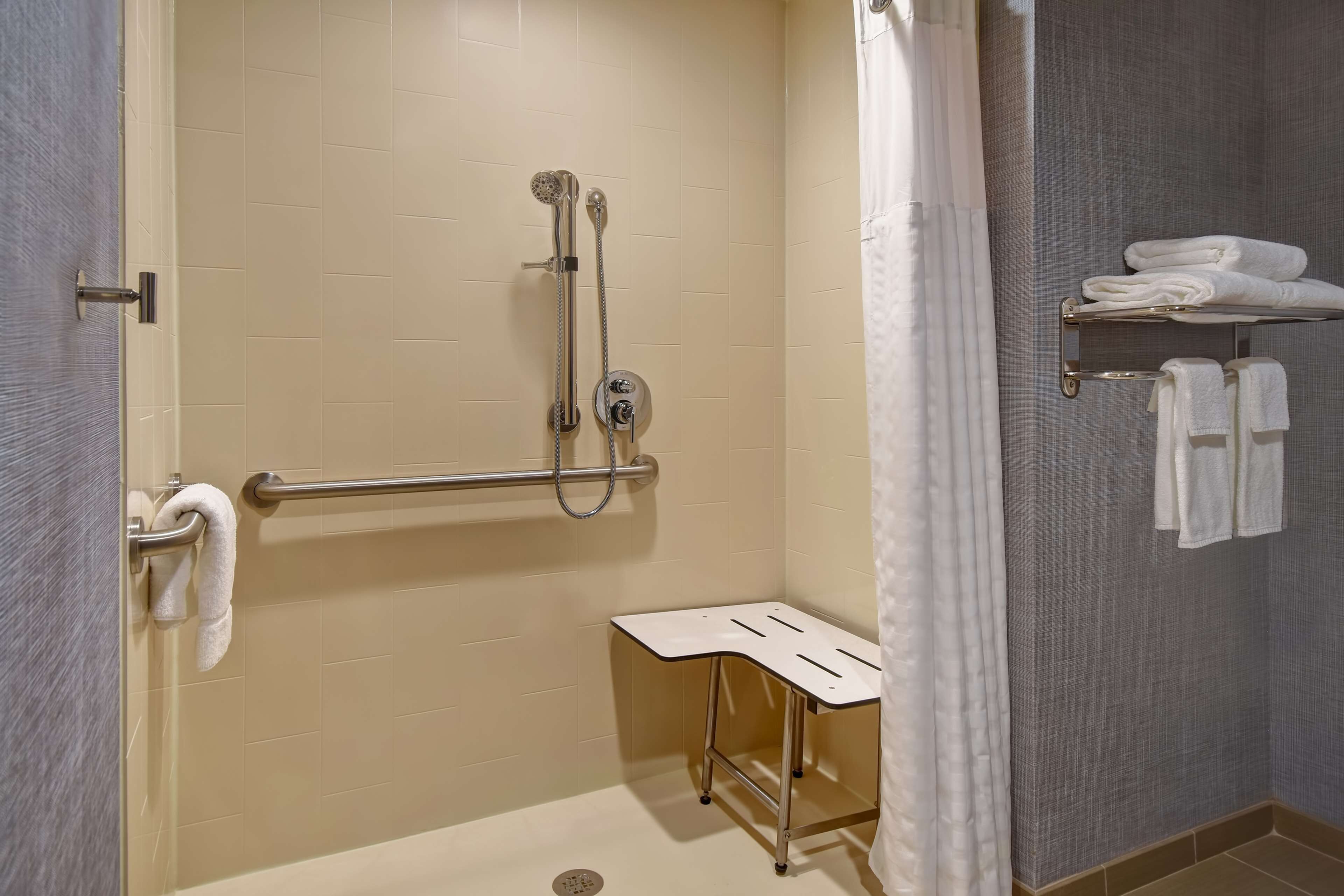 A bathroom with a shower, grab bar, towel rack, and a small table.