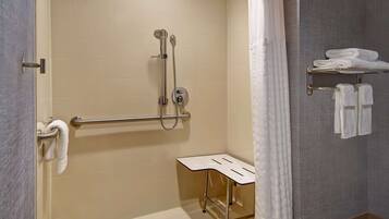 A bathroom with a shower, grab bar, towel rack, and a small table.