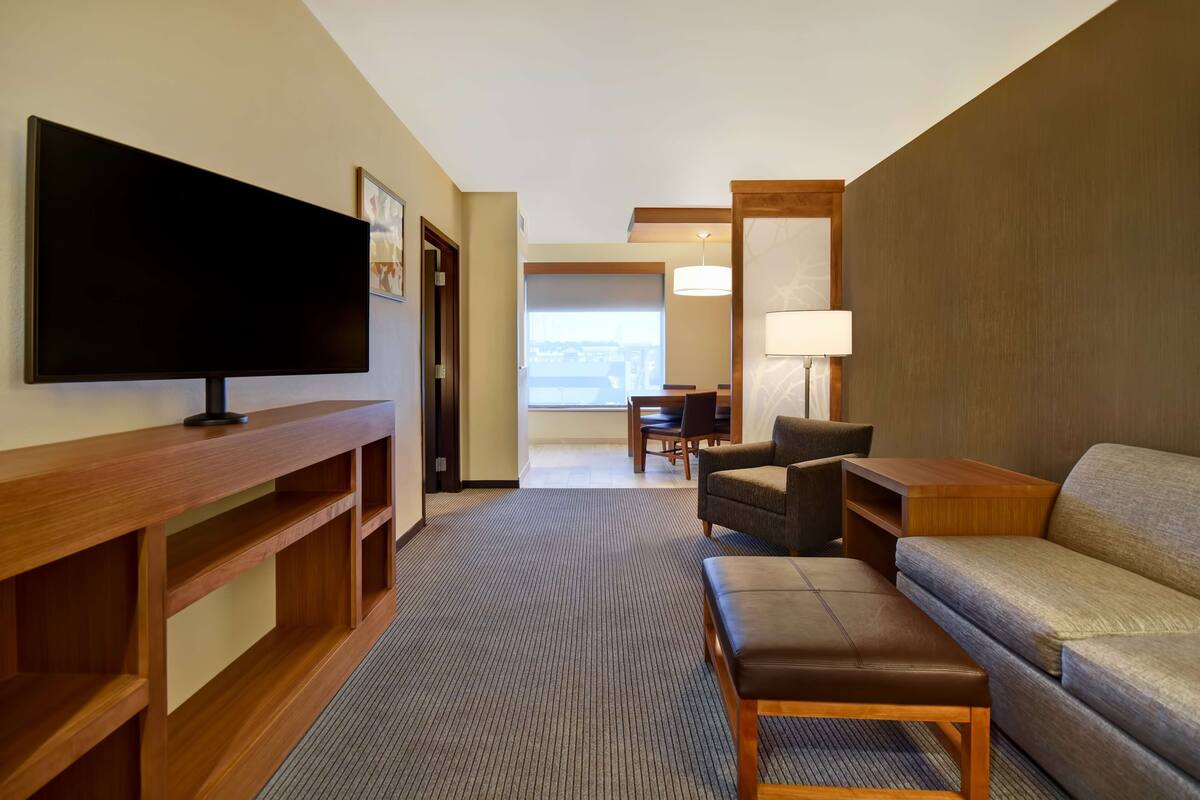 A hotel room with a flat-screen TV, a sofa, a chair, a wooden console table, and a lamp.