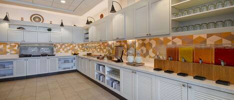 A modern kitchen with white cabinets, a tiled backsplash, and a breakfast bar with juice dispensers.