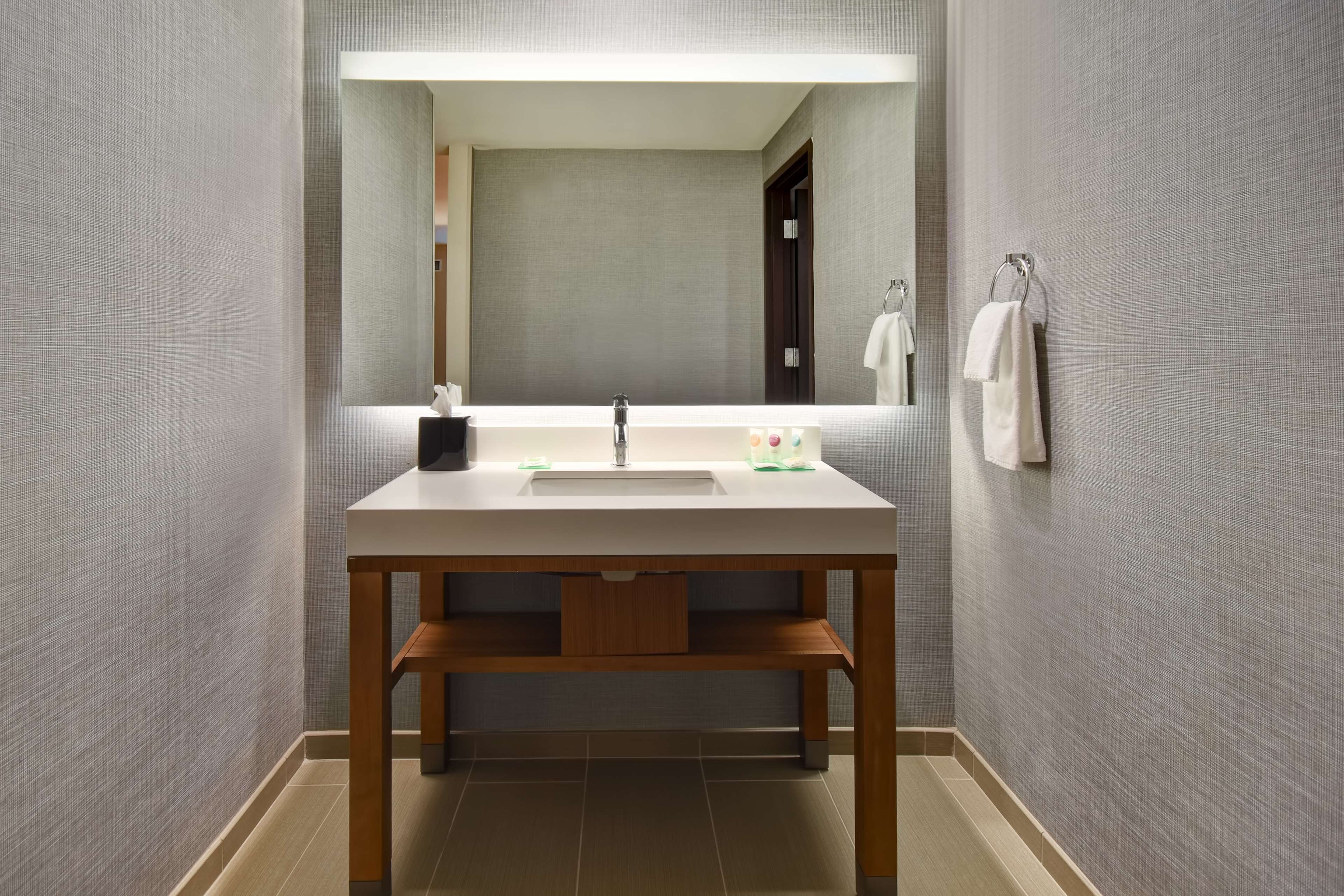A modern bathroom with a wooden vanity, a large mirror, and a wall-mounted towel rack.
