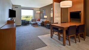 Een moderne hotelkamer met een eethoek, een zithoek, een televisie en een groot raam met uitzicht op de omgeving.