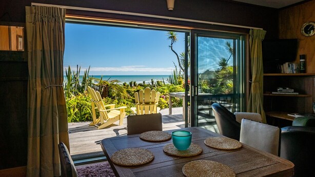 Ein Essbereich mit Tisch für zwei Personen, Blick aufs Meer und eine Holzterrasse mit Stühlen.