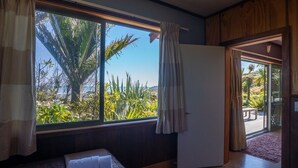 A bedroom with a large window, a bed, and a door leading to a balcony. - Two bedroom cottage with sea views, Punakaiki (Punakaiki)
