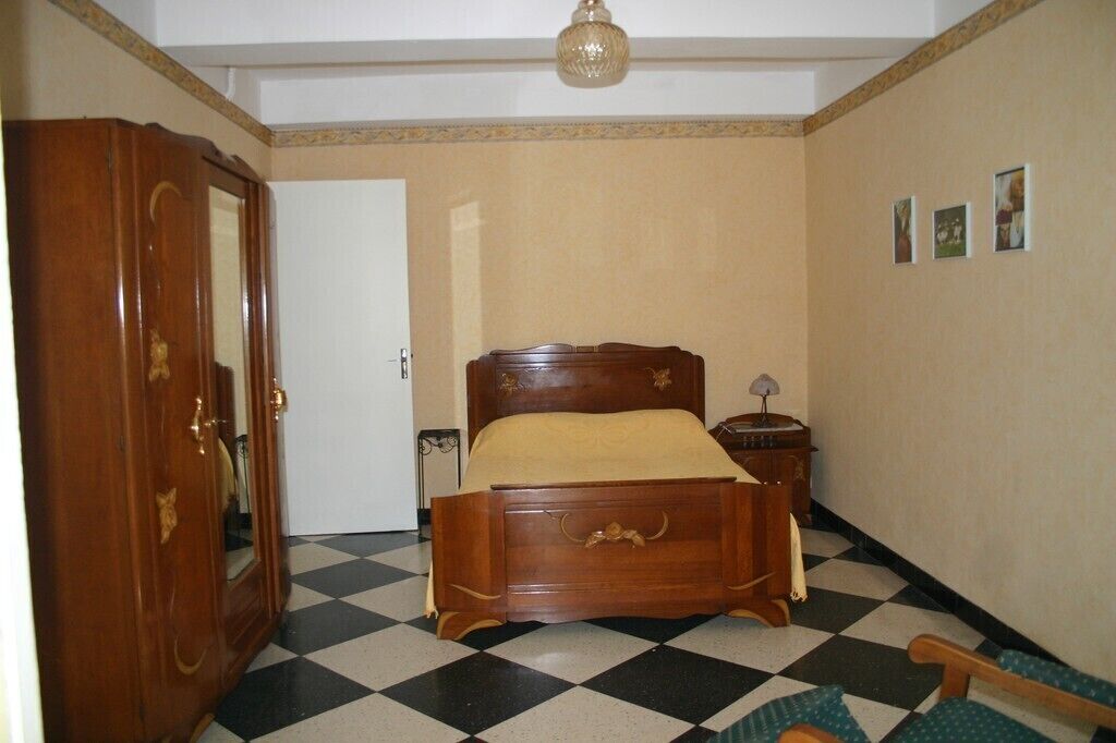 Une chambre avec un lit en bois, une table de chevet, un miroir et un sol à carreaux.