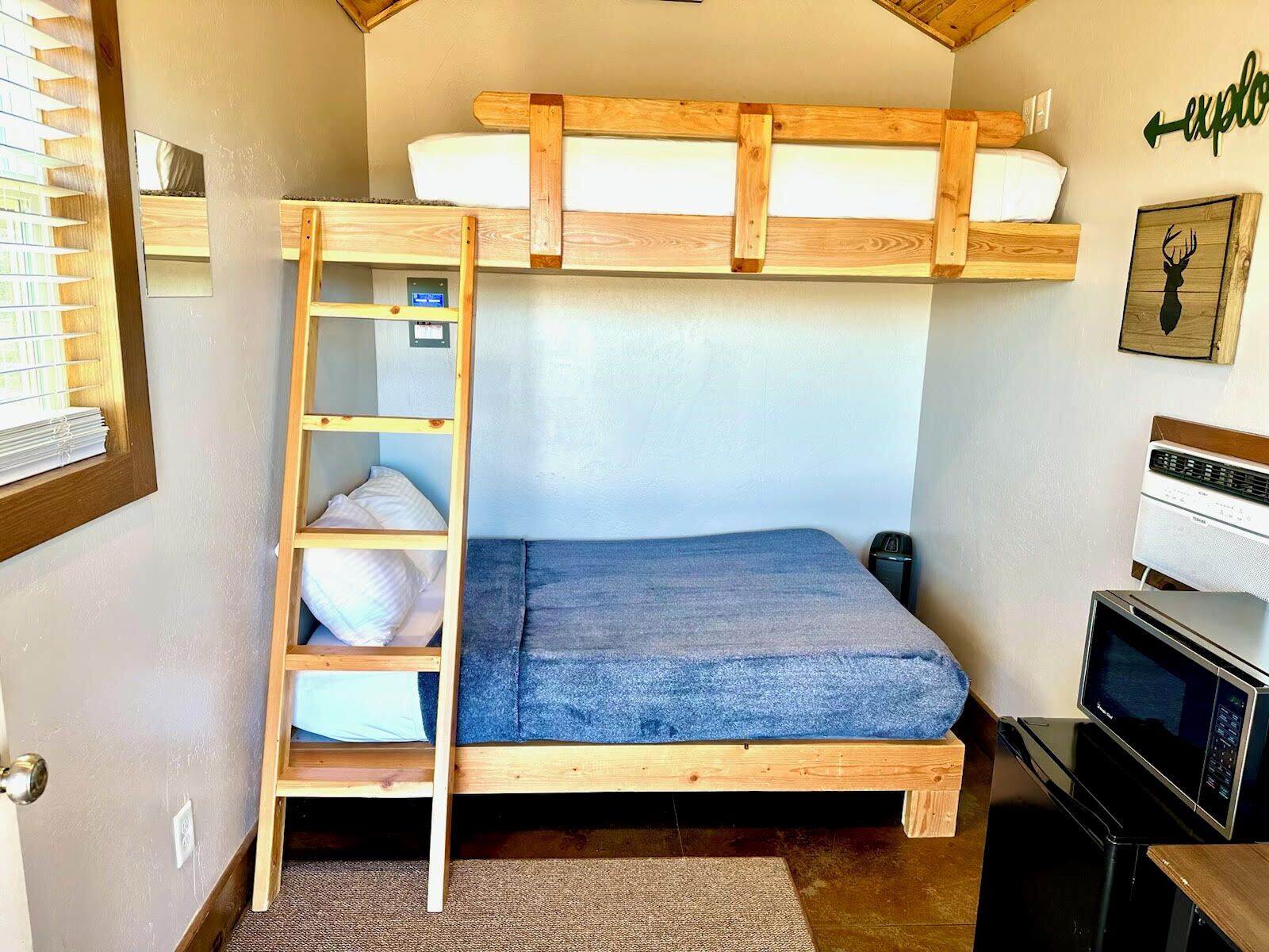 A compact room with a bunk bed, a ladder, a microwave, and a small desk.