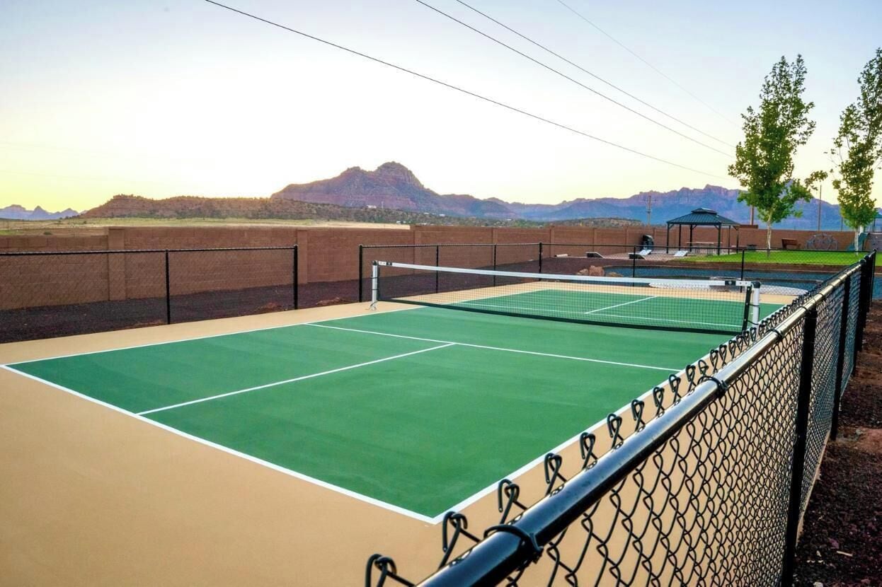 A tennis court with a net, surrounded by a chain-link fence, and mountains in the background.