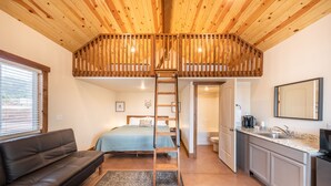 A compact room with a loft bed, a sofa, a kitchen area, and a bathroom. - Gooseberry Lodges (Hurricane)
