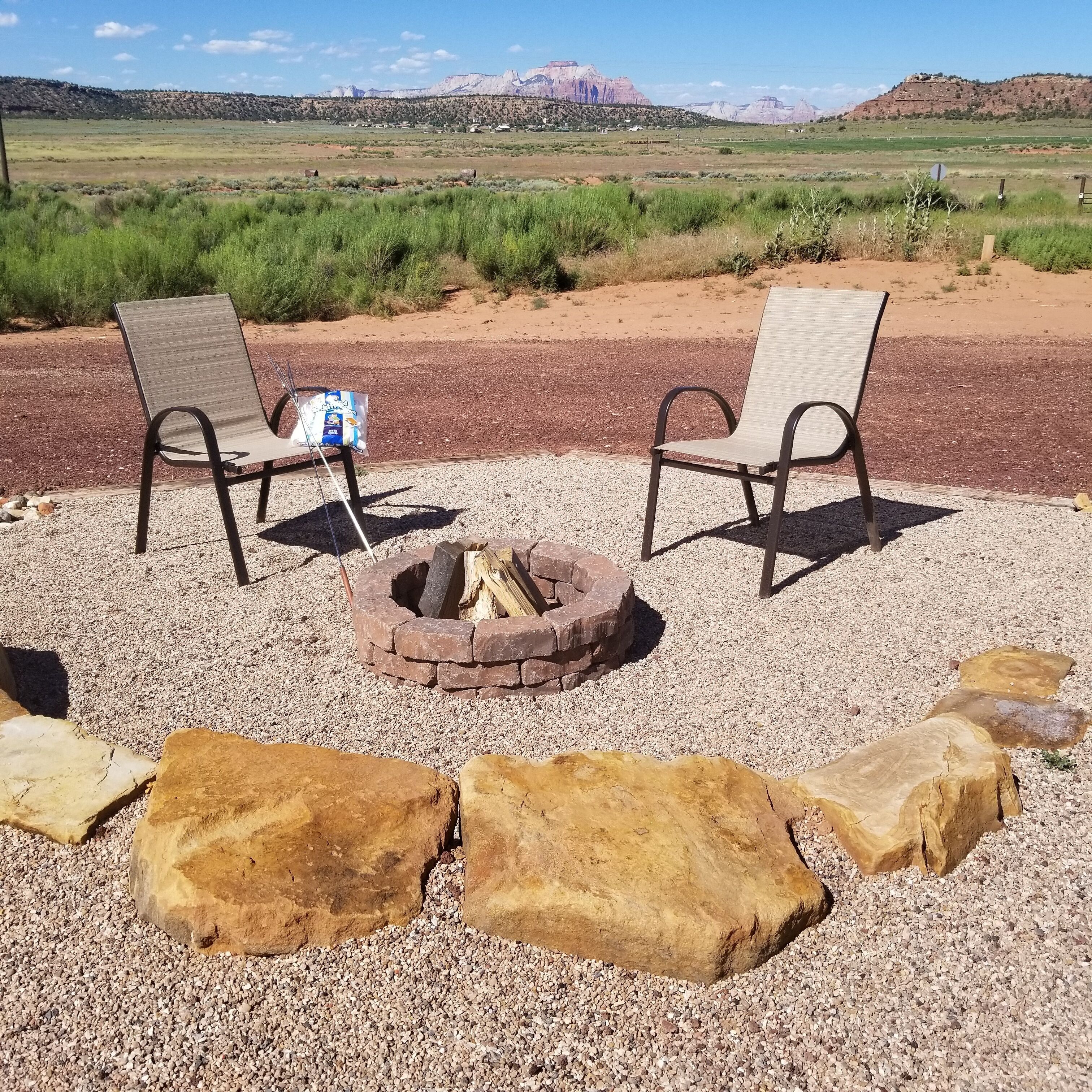 Two metal chairs with a fire pit between them, surrounded by rocks and gravel.