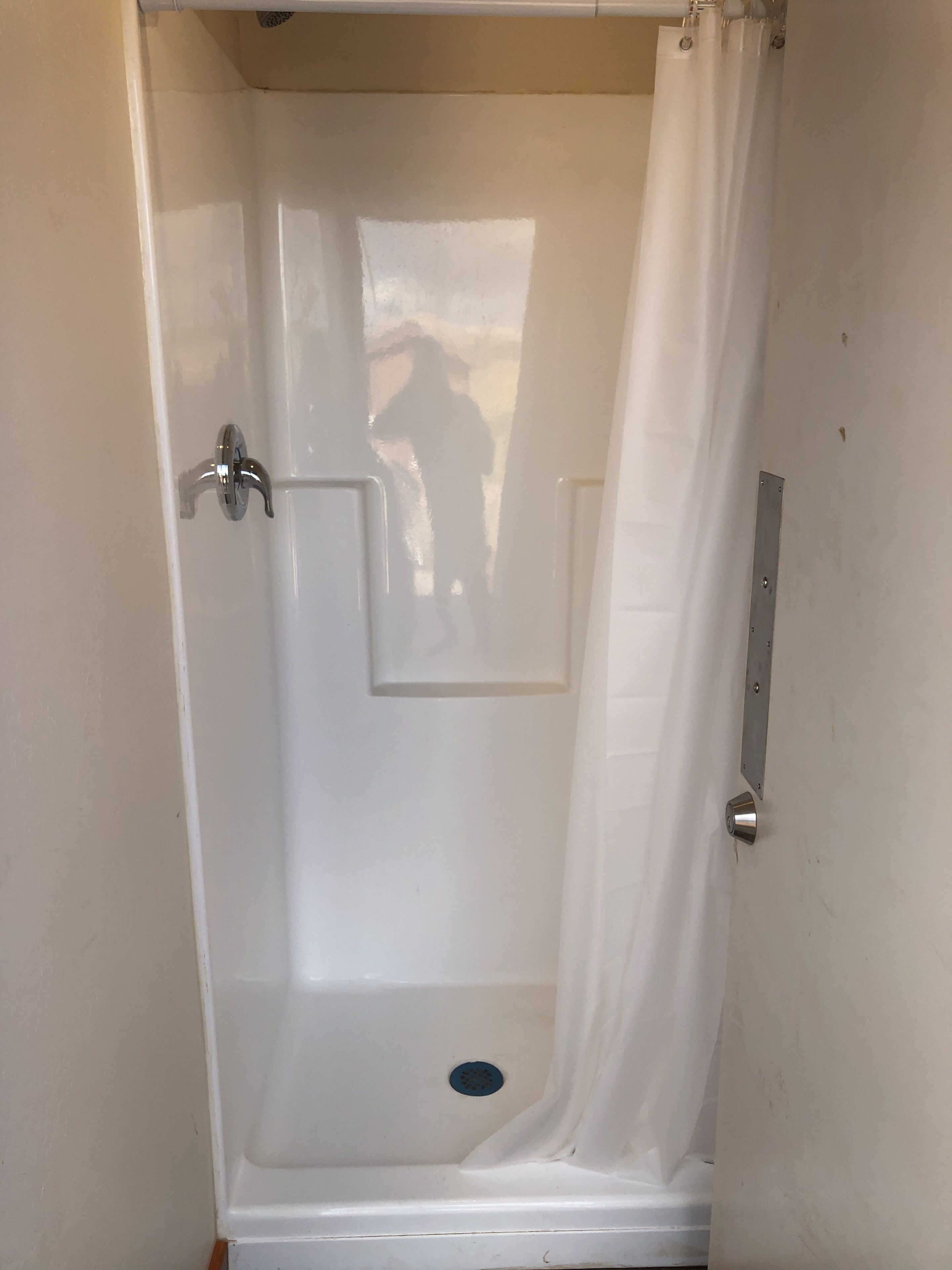 A small, enclosed shower area with a white door and a metal handle.