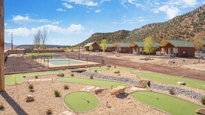 A golf course with bunkers and a putting green, surrounded by wooden cabins with green roofs.